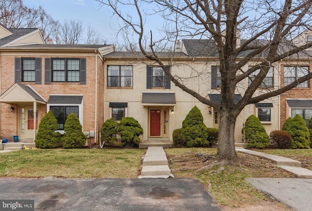 multi unit property with a front lawn, brick siding, roof with shingles, and stucco siding