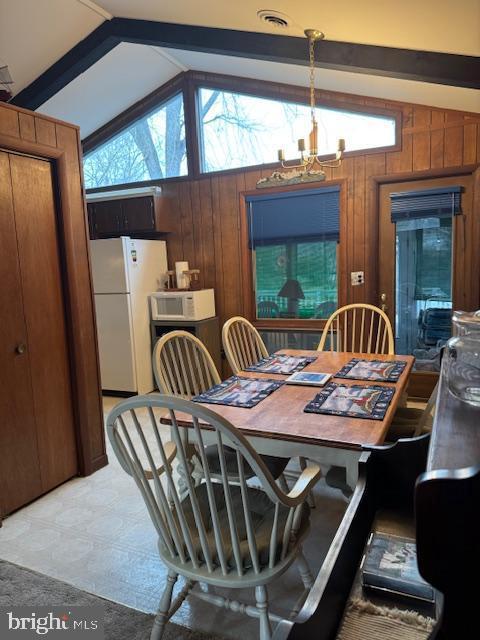 dining room featuring a notable chandelier, plenty of natural light, wooden walls, and vaulted ceiling with beams