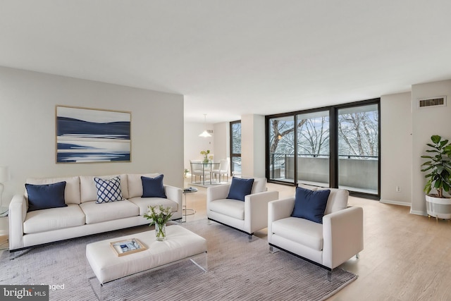 living room with expansive windows, visible vents, baseboards, and wood finished floors