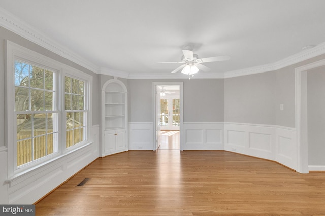 empty room featuring visible vents, light wood-style flooring, crown molding, and a healthy amount of sunlight