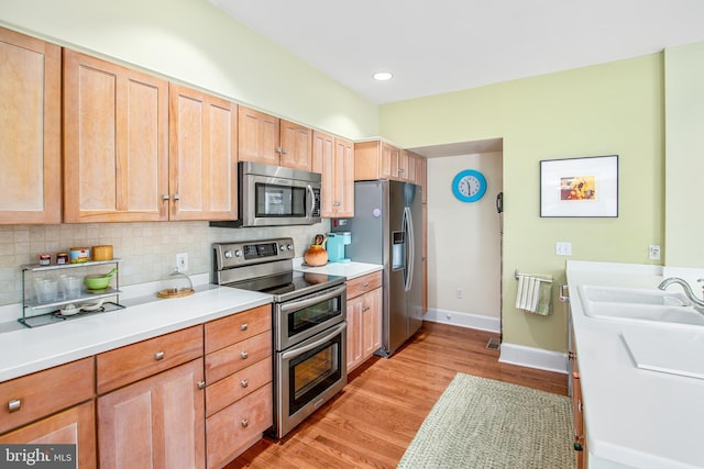 kitchen with light brown cabinetry, sink, backsplash, stainless steel appliances, and light hardwood / wood-style flooring