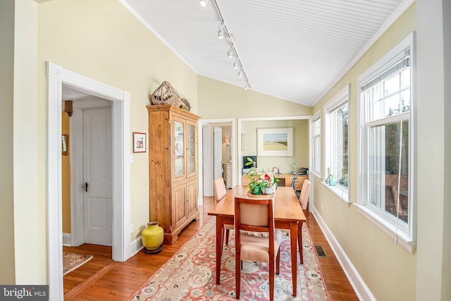 dining space with ornamental molding, lofted ceiling, rail lighting, and wood-type flooring