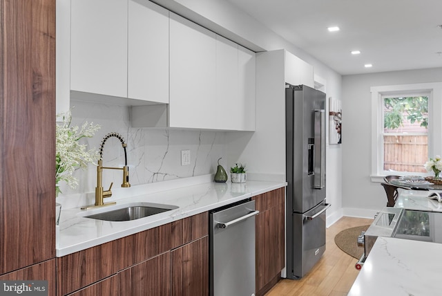 kitchen featuring sink, white cabinetry, stainless steel appliances, light stone countertops, and decorative backsplash