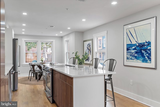 kitchen with high end stainless steel range oven, an island with sink, a breakfast bar area, and light hardwood / wood-style flooring