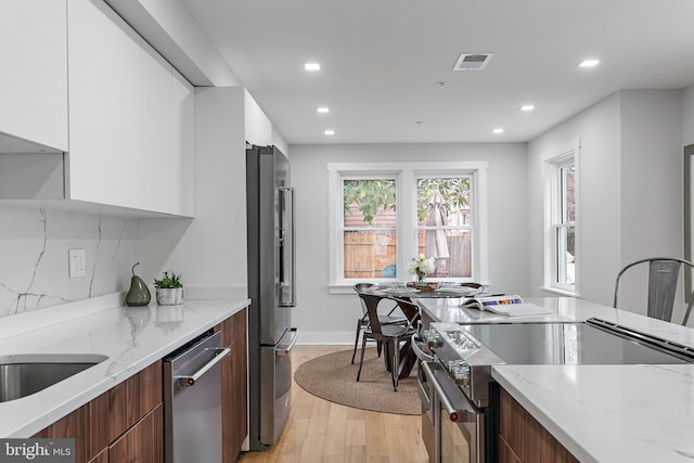 kitchen with white cabinetry, appliances with stainless steel finishes, light stone countertops, and light hardwood / wood-style flooring