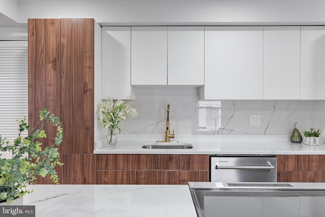 kitchen featuring light stone countertops, sink, white cabinets, and backsplash