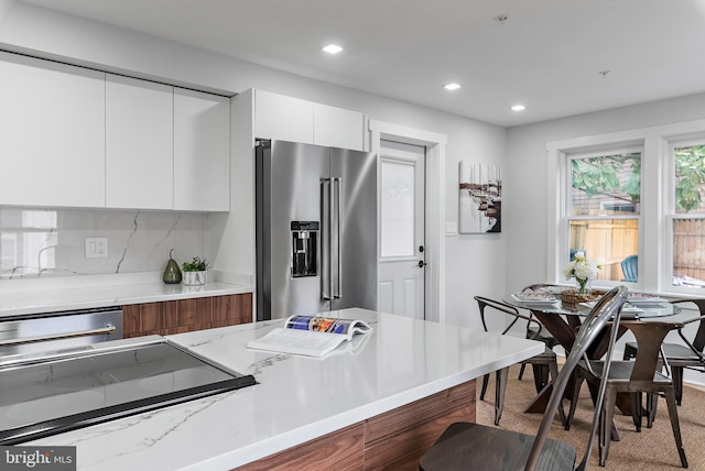 kitchen with a breakfast bar area, stovetop, white cabinetry, high quality fridge, and decorative backsplash