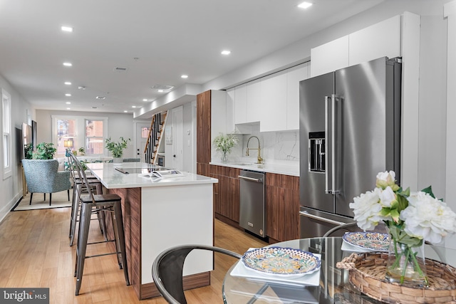 kitchen with sink, backsplash, stainless steel appliances, white cabinets, and a center island with sink