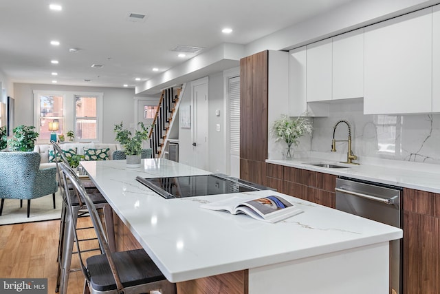 kitchen with sink, a breakfast bar area, white cabinetry, a kitchen island, and light hardwood / wood-style floors