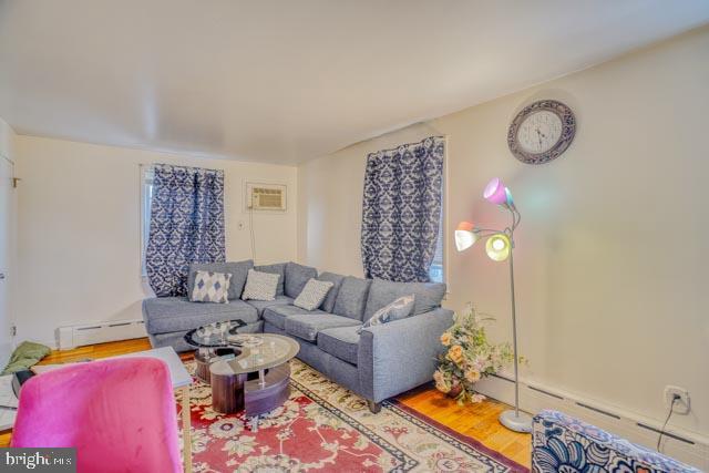 living area featuring a baseboard heating unit, a wall mounted AC, and wood finished floors