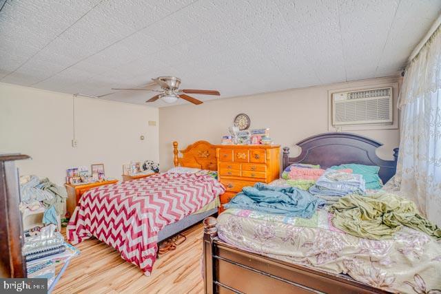 bedroom featuring a textured ceiling, a wall unit AC, wood finished floors, and a ceiling fan