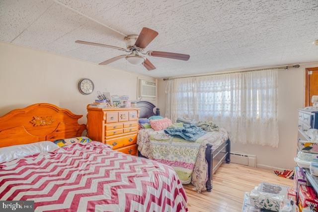 bedroom featuring a textured ceiling, baseboard heating, wood finished floors, and a ceiling fan