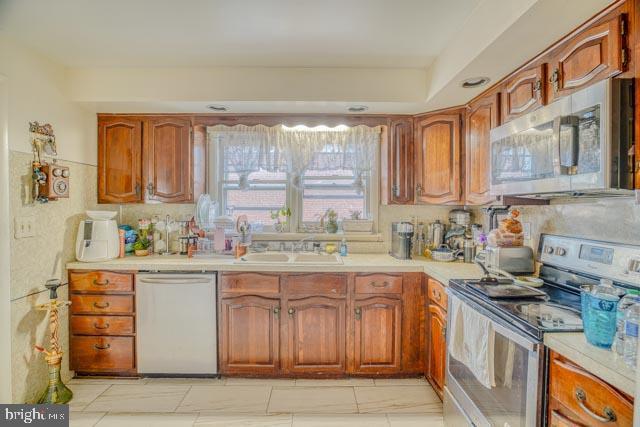 kitchen with light countertops, appliances with stainless steel finishes, a sink, and brown cabinets