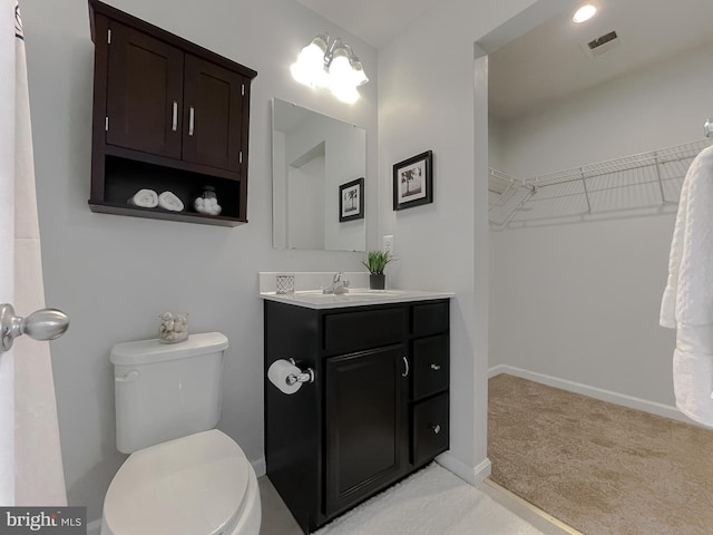 bathroom with visible vents, a spacious closet, toilet, vanity, and baseboards