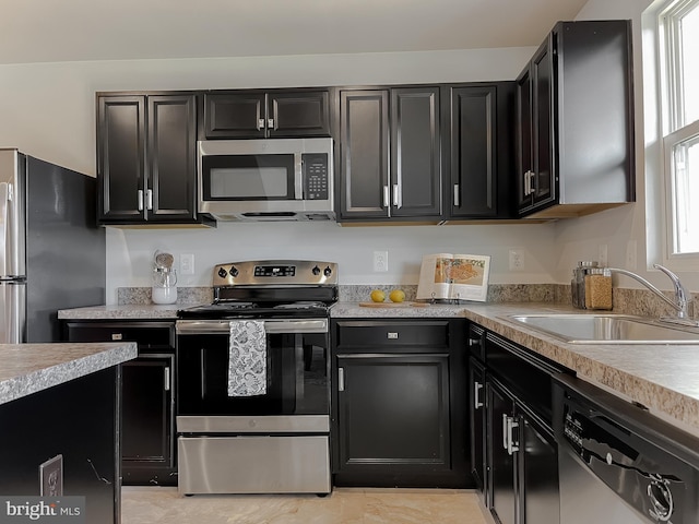 kitchen featuring light countertops, appliances with stainless steel finishes, a sink, and dark cabinets