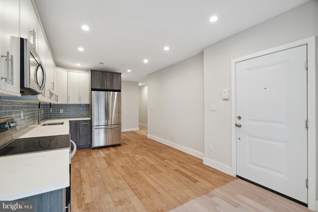 kitchen with tasteful backsplash, sink, white cabinets, stainless steel appliances, and light hardwood / wood-style flooring