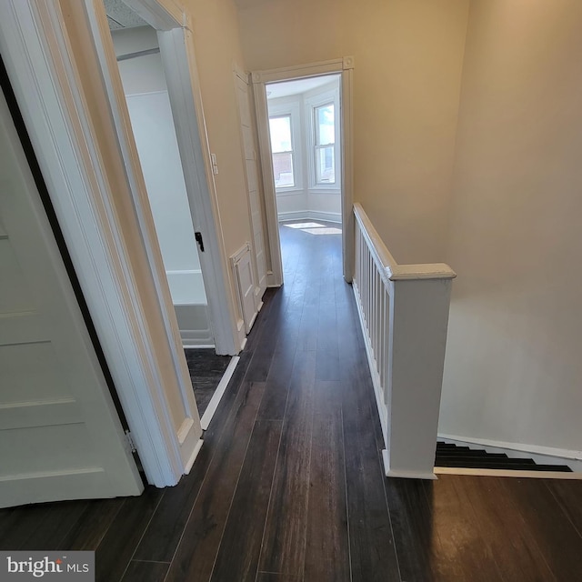 corridor featuring baseboards, dark wood finished floors, and an upstairs landing