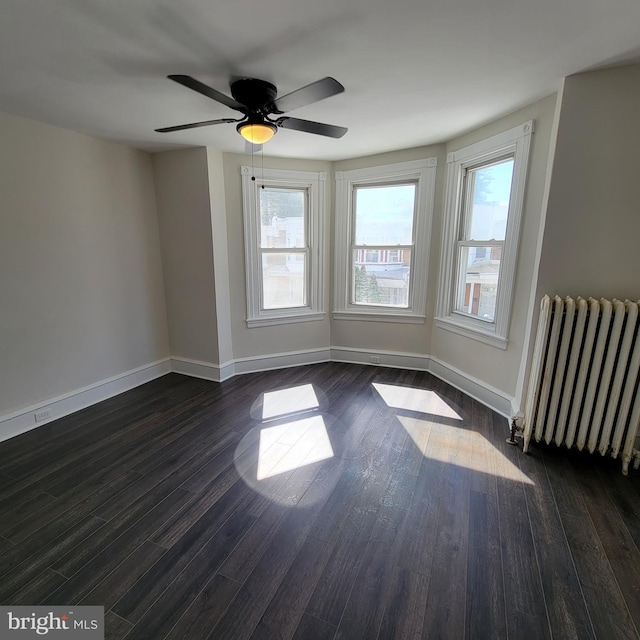 spare room with radiator, baseboards, ceiling fan, and dark wood-style flooring