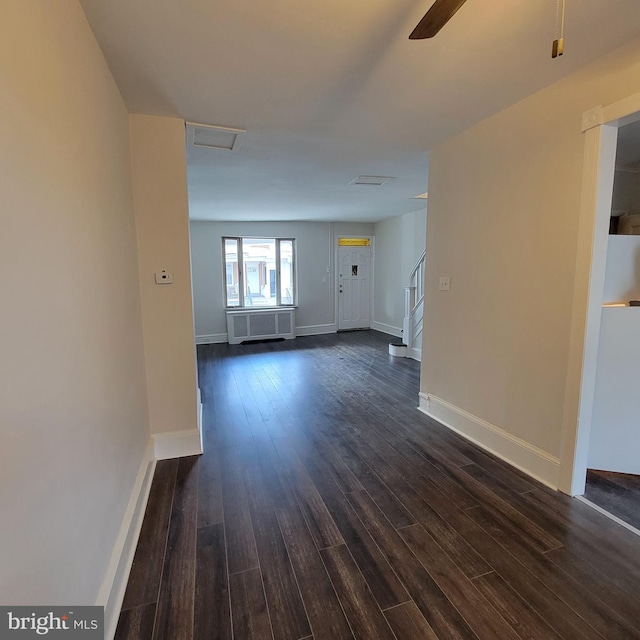 unfurnished living room with dark wood-style floors, baseboards, stairway, and radiator heating unit