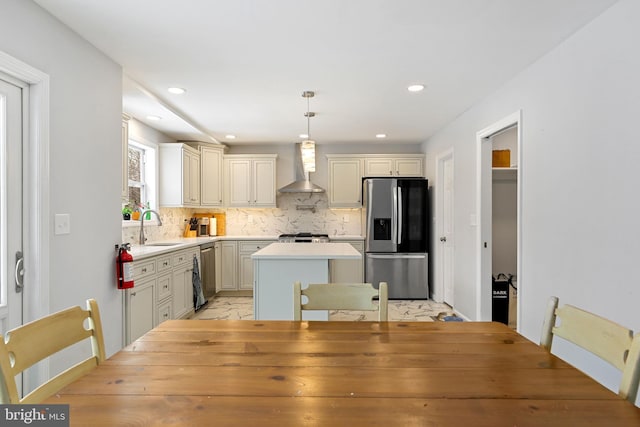 kitchen featuring decorative backsplash, appliances with stainless steel finishes, a center island, wall chimney range hood, and a sink