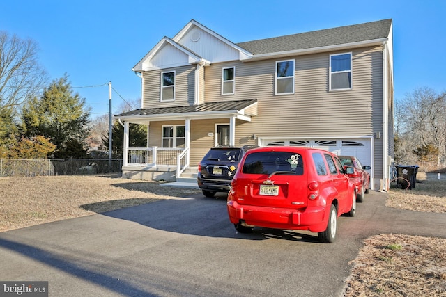 view of front facade with covered porch, aphalt driveway, a standing seam roof, and fence