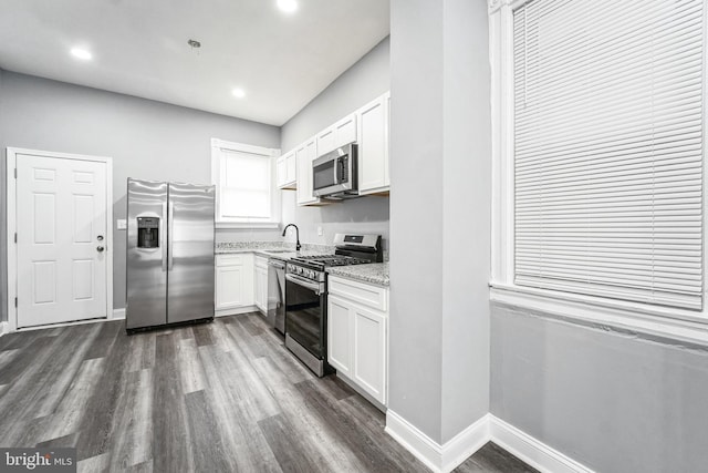 kitchen featuring stainless steel appliances, sink, light stone counters, dark wood-type flooring, and white cabinets