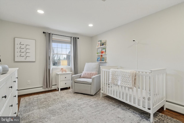 bedroom with a crib, a baseboard radiator, and wood-type flooring