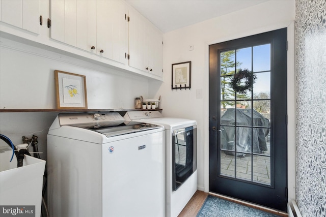 laundry room with sink, washing machine and dryer, cabinets, and light wood-type flooring