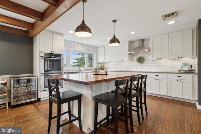 kitchen with white cabinetry, wall chimney range hood, double oven, and hanging light fixtures