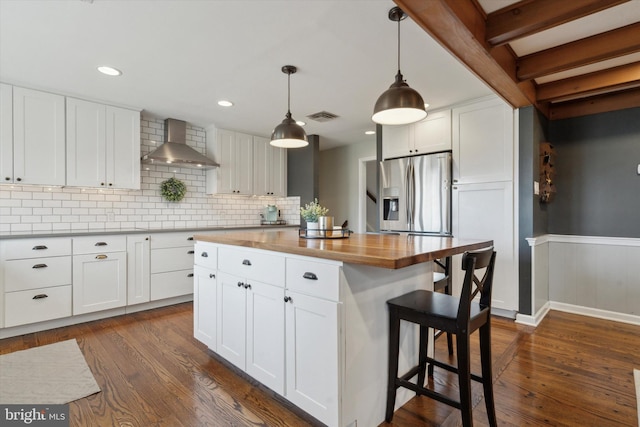 kitchen featuring white cabinets, stainless steel fridge, decorative light fixtures, and wall chimney range hood