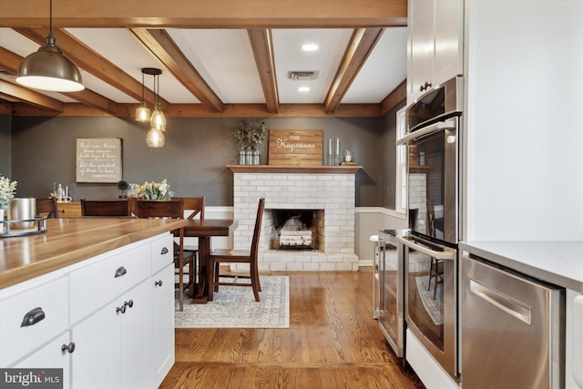 kitchen with appliances with stainless steel finishes, white cabinets, hanging light fixtures, light hardwood / wood-style floors, and beam ceiling