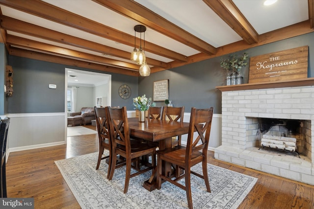 dining space featuring wood-type flooring, a fireplace, and beam ceiling