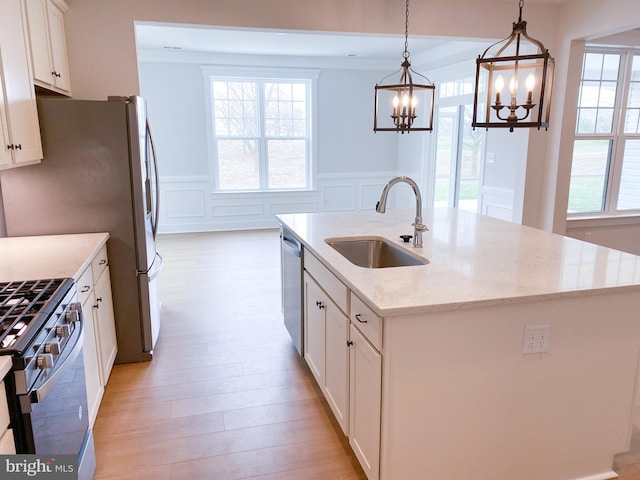 kitchen with sink, light stone counters, hanging light fixtures, a center island with sink, and stainless steel appliances