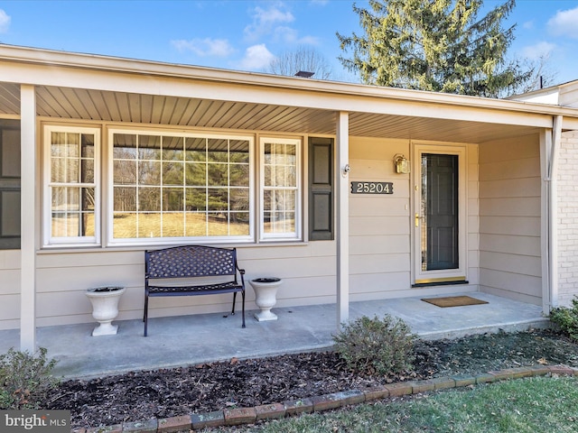 doorway to property featuring covered porch and brick siding