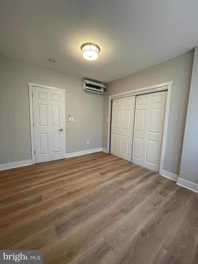 unfurnished bedroom with wood-type flooring, an AC wall unit, and a closet