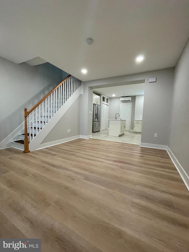 unfurnished living room featuring a wall mounted AC, sink, and light wood-type flooring