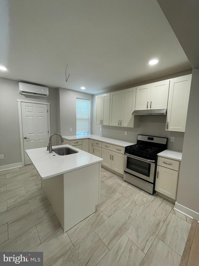 kitchen with stainless steel range with gas cooktop, sink, a wall mounted AC, white cabinets, and a kitchen island with sink