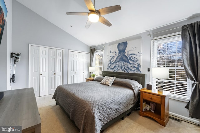 carpeted bedroom featuring multiple closets, lofted ceiling, visible vents, and a ceiling fan