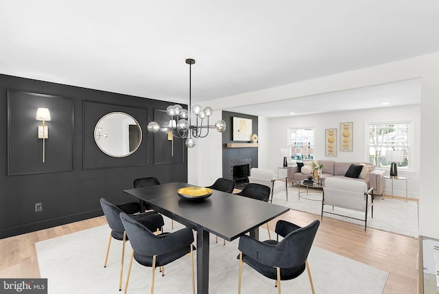 dining area with a brick fireplace, a chandelier, and light wood-type flooring