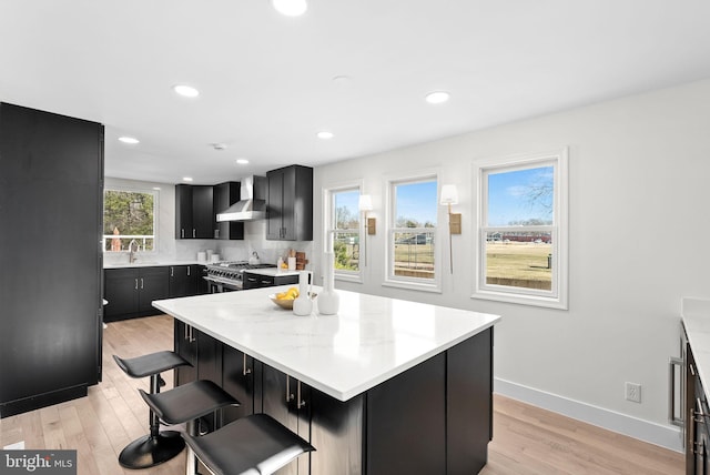 kitchen featuring stainless steel stove, light hardwood / wood-style flooring, a breakfast bar, a center island, and wall chimney exhaust hood