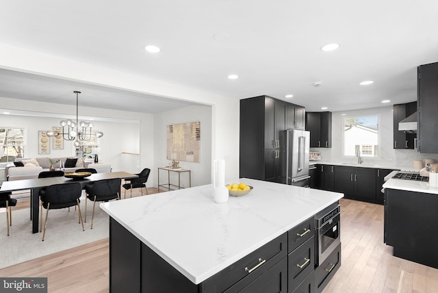 kitchen featuring appliances with stainless steel finishes, a center island, light stone counters, light hardwood / wood-style floors, and wall chimney exhaust hood