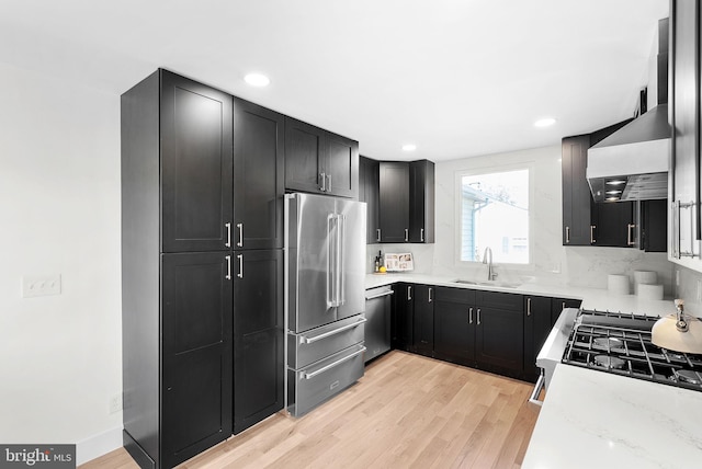 kitchen with wall chimney exhaust hood, sink, light hardwood / wood-style flooring, stainless steel appliances, and light stone countertops