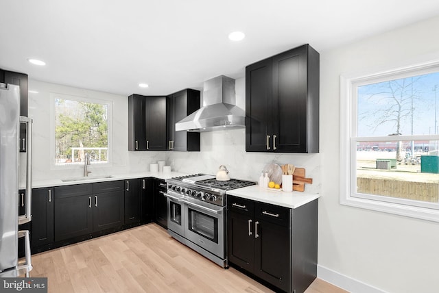 kitchen featuring wall chimney exhaust hood, sink, high quality appliances, light hardwood / wood-style floors, and backsplash