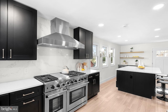 kitchen with a breakfast bar area, tasteful backsplash, a kitchen island, range with two ovens, and wall chimney range hood