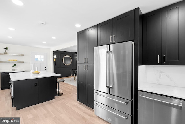 kitchen with a breakfast bar area, tasteful backsplash, light hardwood / wood-style flooring, appliances with stainless steel finishes, and a kitchen island