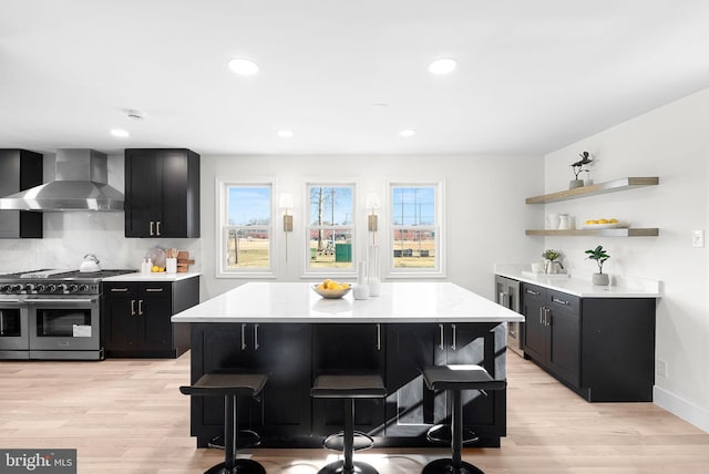 kitchen with wall chimney range hood, double oven range, a breakfast bar area, and a kitchen island