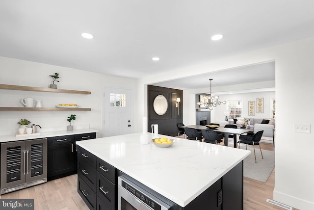 kitchen with wine cooler, stainless steel microwave, light hardwood / wood-style floors, and a kitchen island