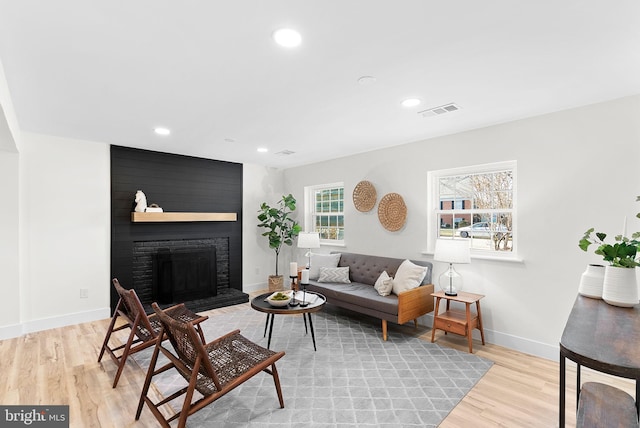 living room with a brick fireplace and light wood-type flooring