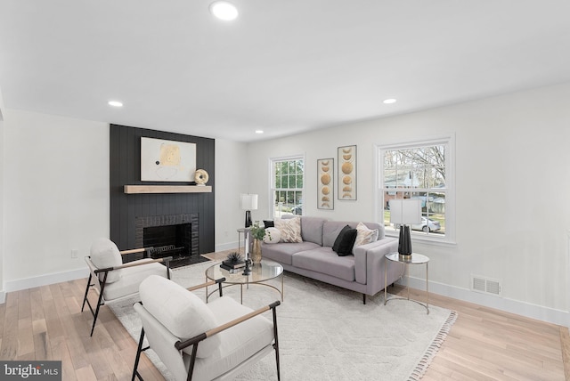 living room with a brick fireplace and light wood-type flooring