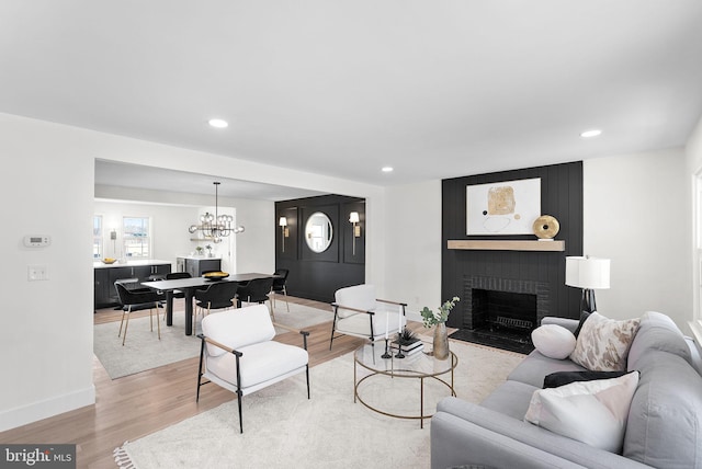 living room featuring a brick fireplace, a notable chandelier, and light hardwood / wood-style flooring